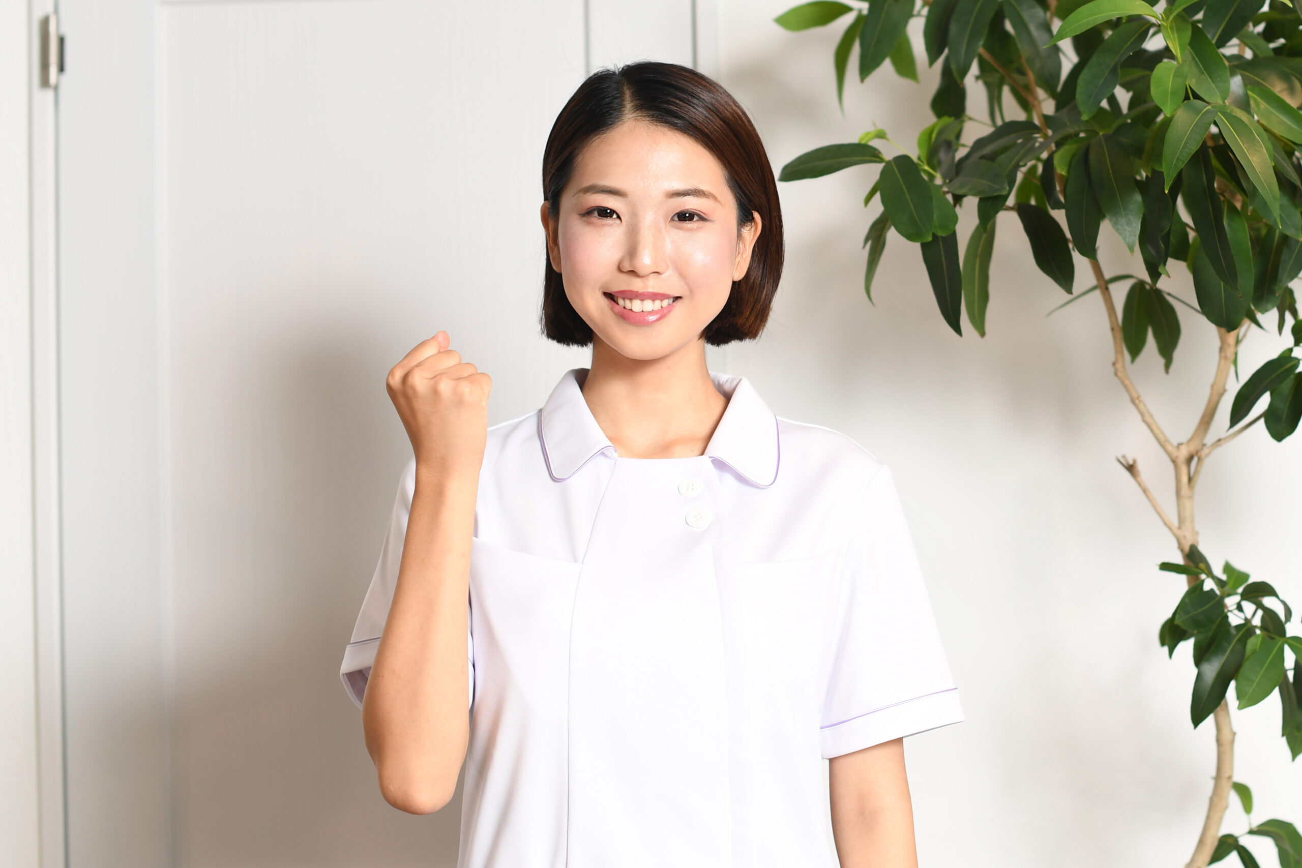 a smiling young asian medical worker wearing a white coat doing a fist pump